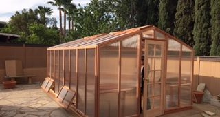 Deluxe redwood and polycarbonate greenhouse kit on backyard patio.