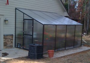 Aluminum lean-to greenhouse kit with polycarbonate paneling and flowers inside.