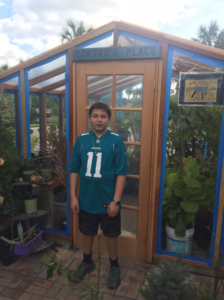 Our customer’s son standing in front of his assembled backyard redwood greenhouse kit.